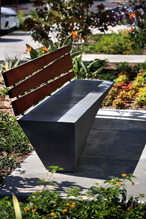 A bench with a wooden slat back and a black slat seat is situated in a garden.
