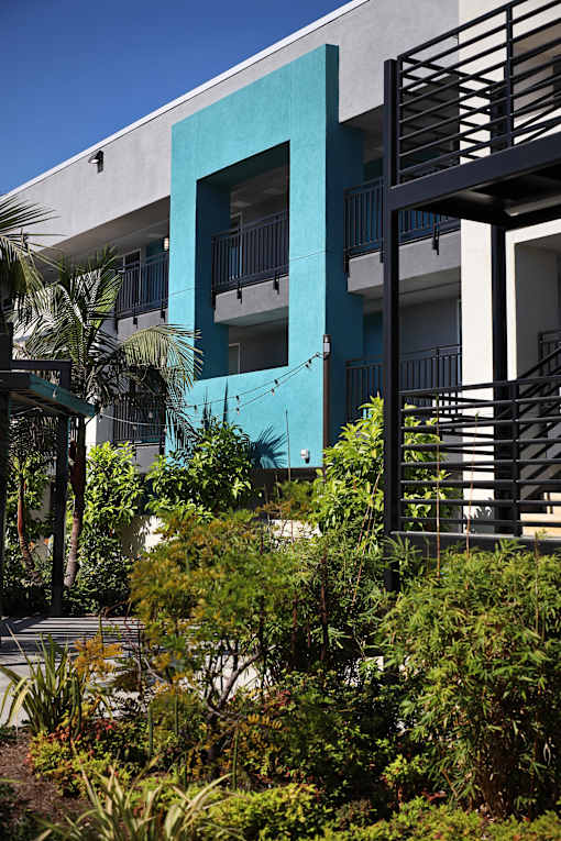 A blue painted building with a balcony and plants in front.