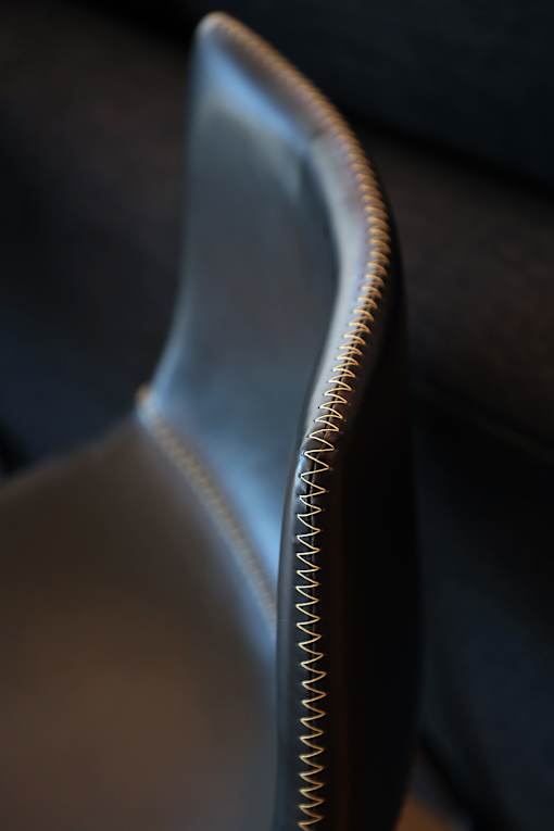 A black chair with a white seat and a brown stitched back.