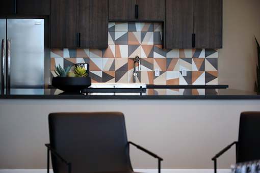 A kitchen with a tile backsplash and two chairs.