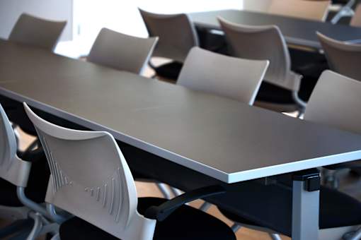 A white plastic chair with a black seat cushion is in front of a table.
