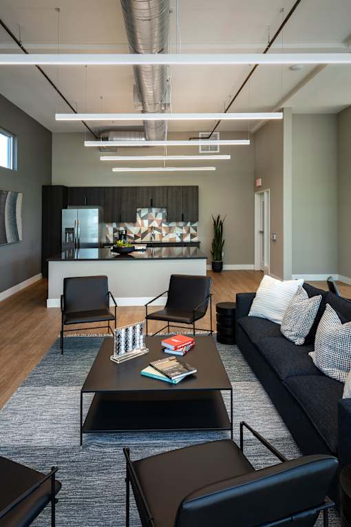 A modern living room with a black couch, a coffee table, and a kitchen area in the background.