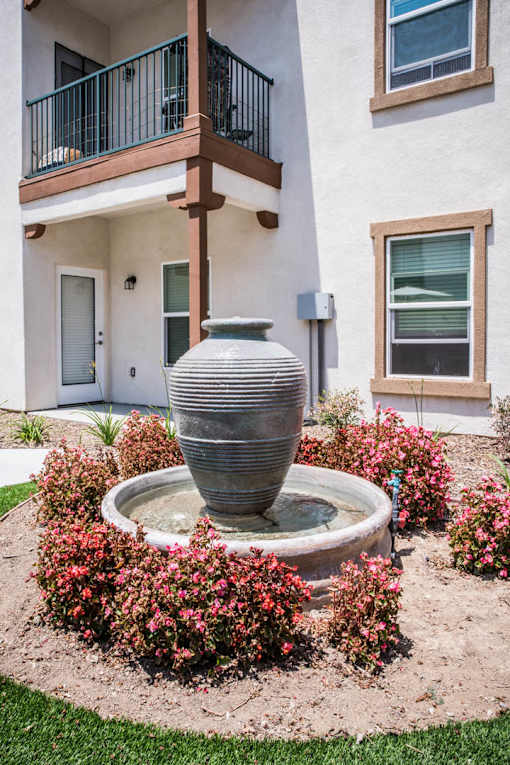 A grey vase is in the middle of a fountain surrounded by pink flowers.