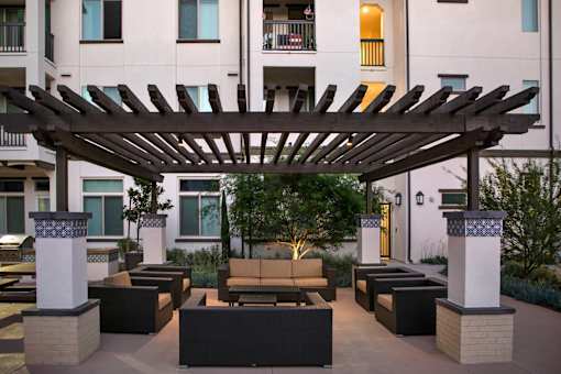 A patio with a wooden pergola and black couches.