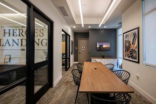 A conference room with a long table and chairs, a television, and a glass wall with the word "HEROES" on it.