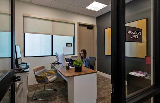 A woman is sitting at a desk in an office with a sign that says "Manager's Office" on the wall behind her.