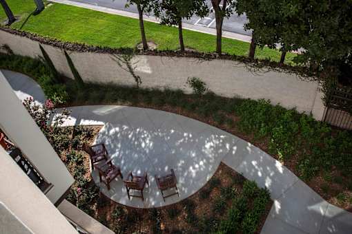A circular patio with chairs and a table is surrounded by a garden.
