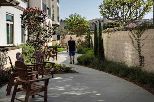A man walks down a sidewalk past a row of wooden chairs.