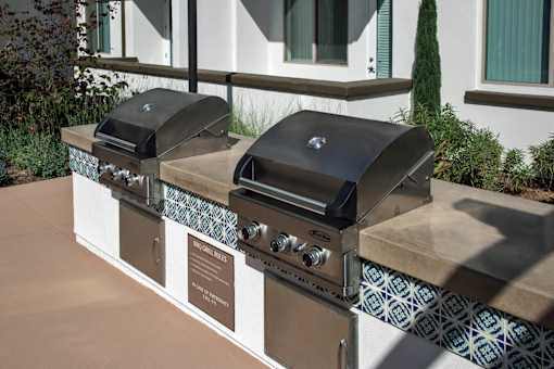 Two black grills on a tan and white outdoor kitchen.