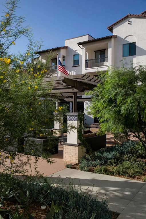 A building with a flag on the balcony is surrounded by greenery.