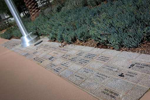 A memorial with names and a hammer is in front of a bush.