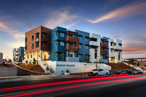 A modern apartment complex named Milejo Village is shown with cars passing by on the street.
