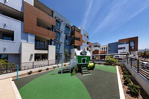 A playground area with a slide and green grass in front of apartment buildings.