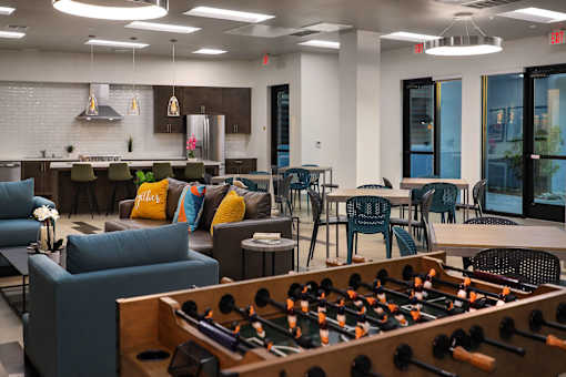 A foosball table is in the foreground of a room with a bar and seating area.