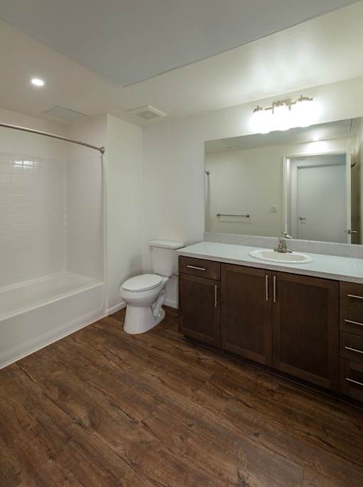 A white toilet sits in a bathroom with wood floors and brown cabinets.