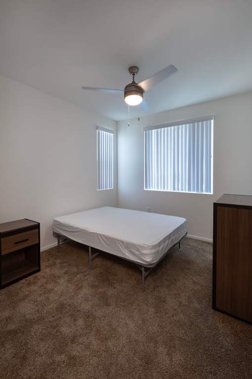 A bedroom with a bed, dresser, and ceiling fan.