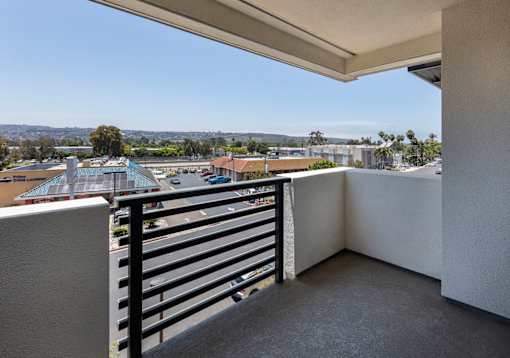 A balcony with a black railing overlooks a parking lot and buildings.