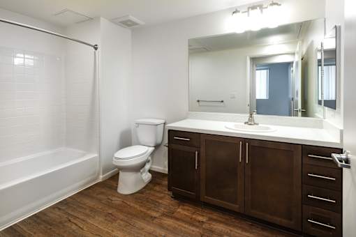 A white toilet sits in a bathroom with wood floors and brown cabinets.