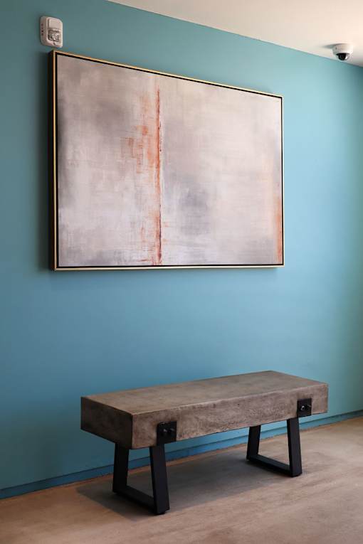 A large abstract painting hangs on a wall above a bench.