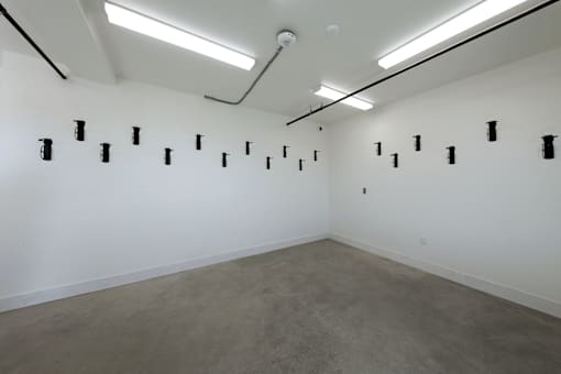 A room with a white wall and a grey floor with black objects on it.