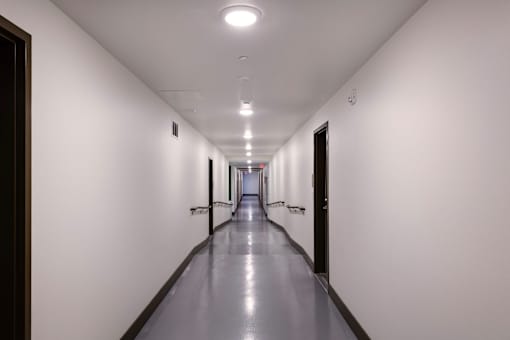 A long, narrow hallway with doors on both sides and recessed lighting on the ceiling.