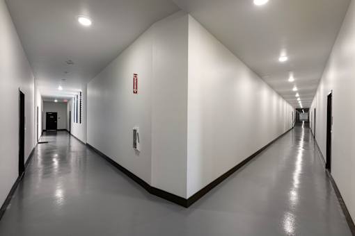 A long hallway with white walls and a red fire extinguisher on the wall.