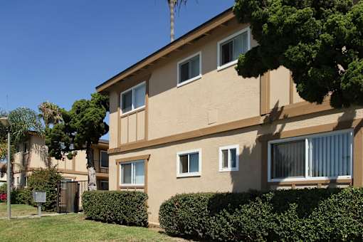 A beige building with a brown roof and a tree in front.