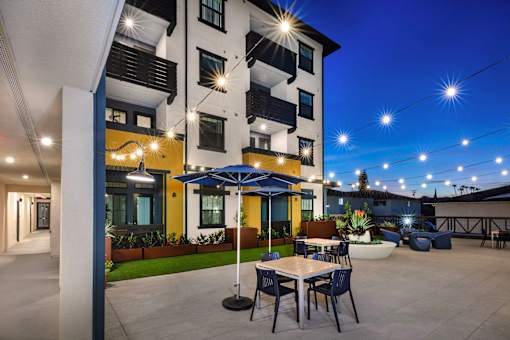 A patio area with tables and chairs is illuminated by lights at night.