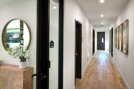 A hallway with a round mirror on the wall and a wooden dresser with a vase of flowers on top.