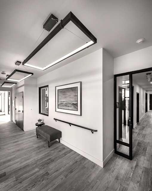 A black and white photo of a hallway with a bench and a painting on the wall.