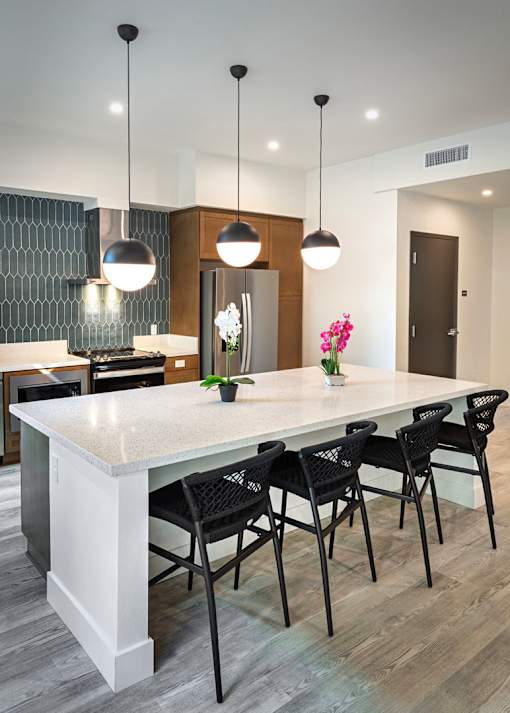 A modern kitchen with a white island and black chairs.