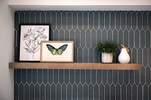 A shelf with a picture of a butterfly, a plant, and a vase.