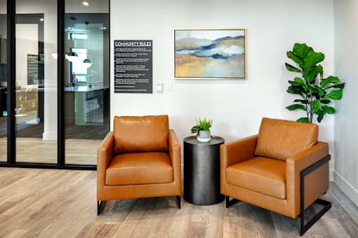 Two brown leather chairs are placed in front of a wall with a framed artwork and a plant.