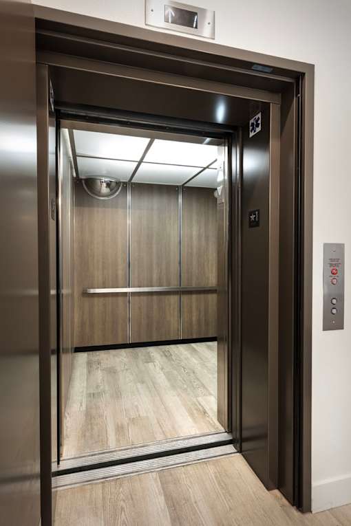 A stainless steel elevator with a glass door and a control panel on the right side.