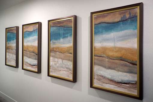 Four paintings of beach scenes are lined up on a wall.