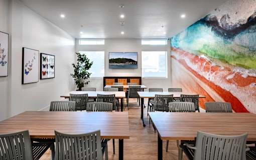 A room with a long table and chairs with a painting on the wall.