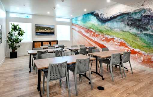 A room with a large painting on the wall and several tables and chairs.