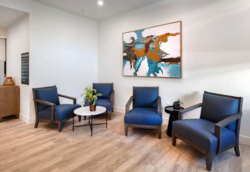 A room with four blue chairs and a painting on the wall.