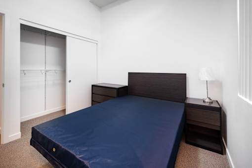A bed with a dark blue cover sits in a room with white walls.