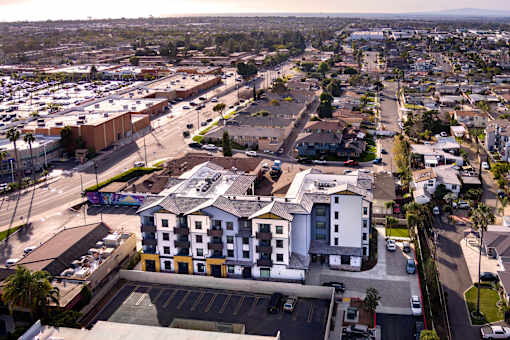 A large white building with a yellow stripe is in the center of a parking lot.