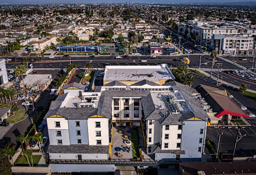 A large white building with a black roof is surrounded by a parking lot.