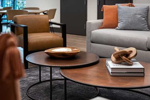 A living room with a grey couch, a brown chair, and a round table with a book and a pretzel on it.