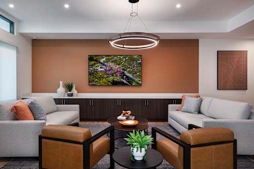A modern living room with a grey sofa, a brown leather armchair, a coffee table with a plant and a painting on the wall.