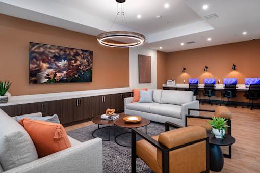 A modern living room with a grey sofa, orange pillow, and a painting on the wall.