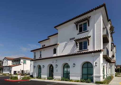 A white building with a red roof and a balcony on the second floor.
