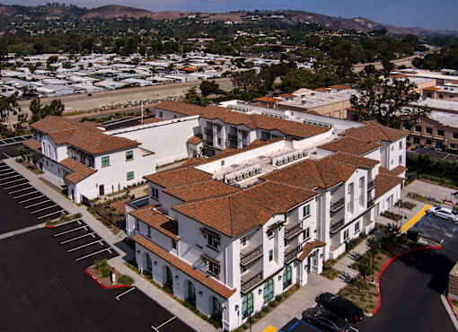 A large white building with a red roof is surrounded by a parking lot.