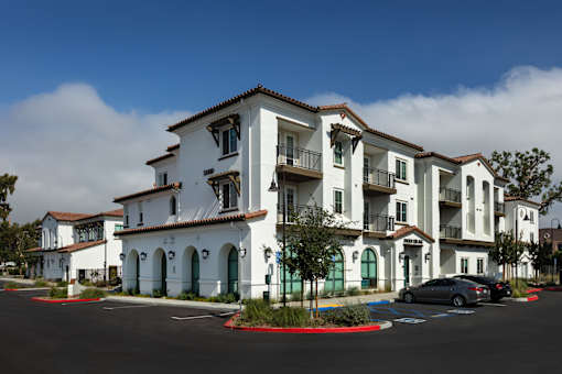 A row of white buildings with balconies and green doors.