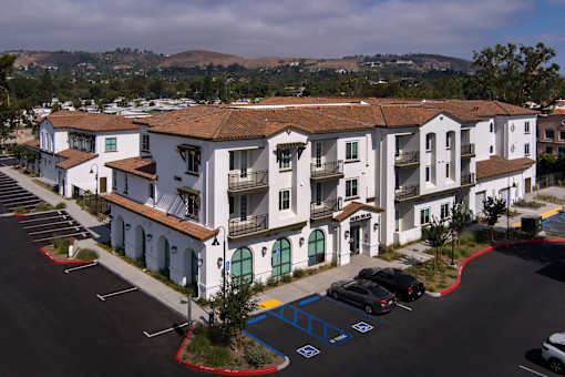 A parking lot in front of a white building with a red roof.