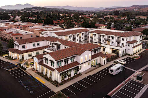 A parking lot in front of a white building with a red roof.