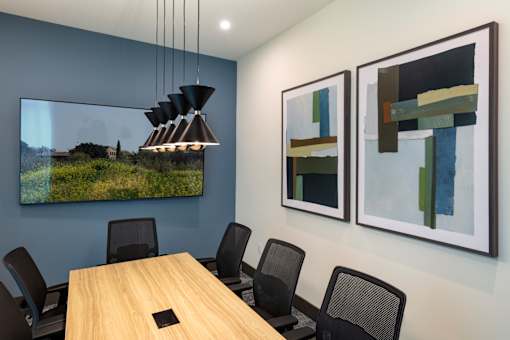 A conference room with a long table and chairs, a hanging light fixture, and two abstract paintings on the wall.